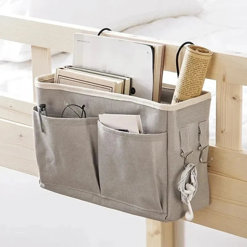 A beige fabric storage rack mounted on a wooden bed frame holding various papers and a rolled-up cloth item.