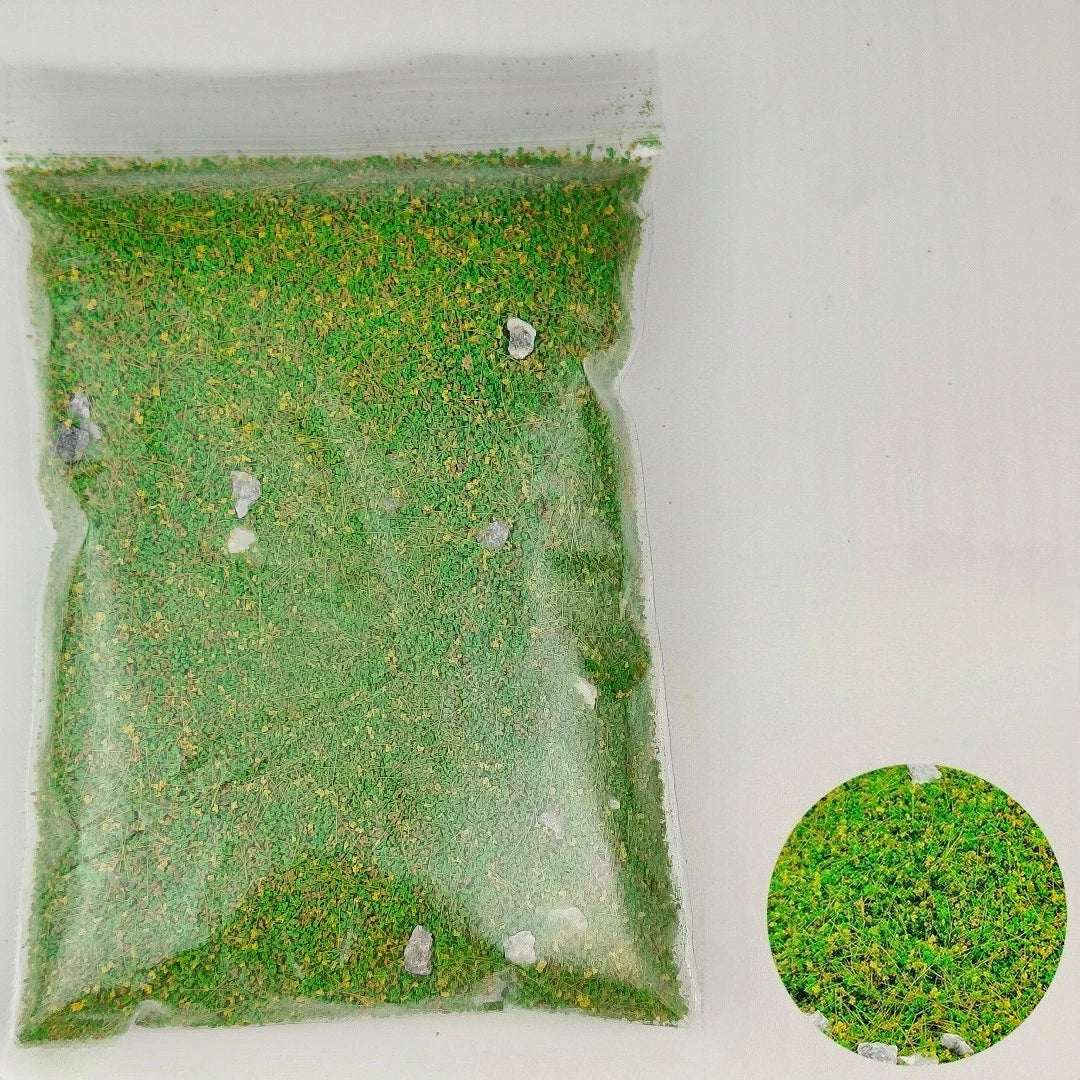 A clear plastic bag filled with a DIY miniature landscape kit containing green simulated grass and small stones.