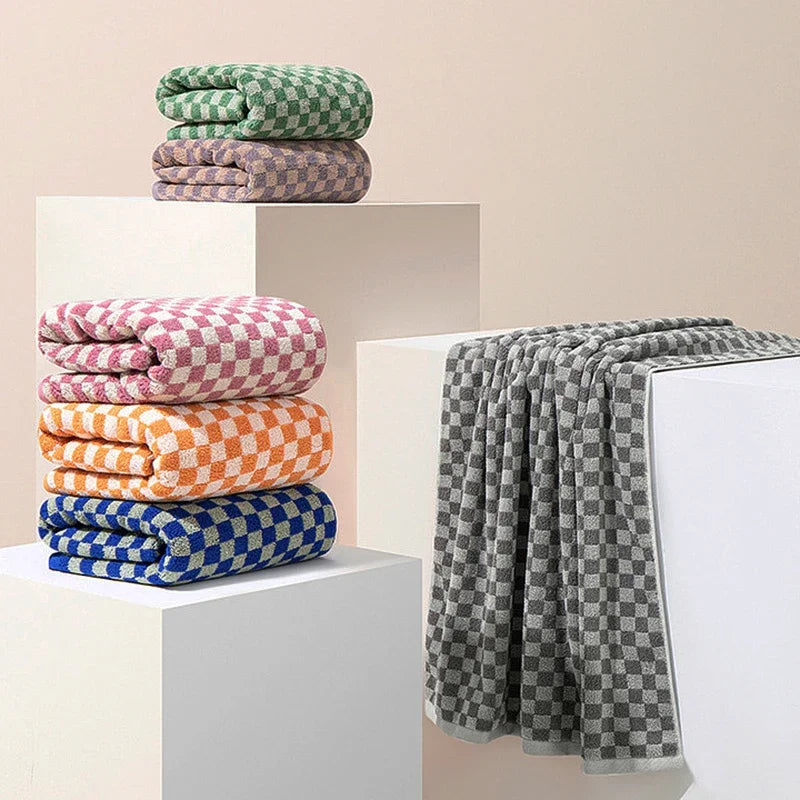 A set of plaid cotton bath towels in shades of green, purple, and orange stacked on white display stands.