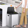 A person is opening a dual compartment stainless steel trash can in a kitchen setting.