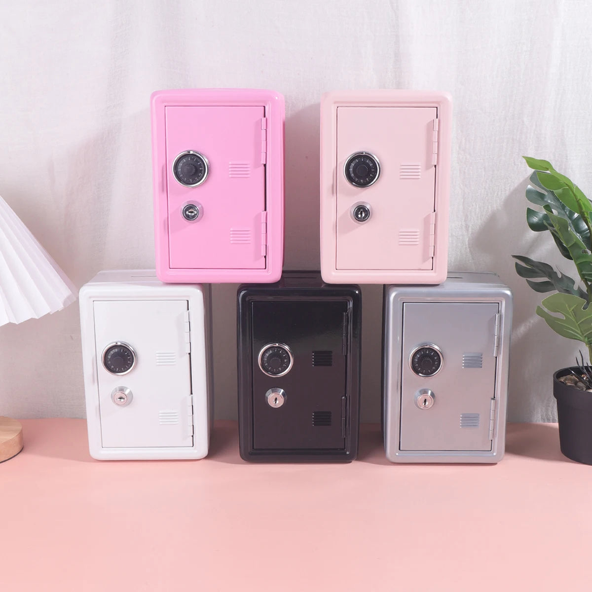 A set of five solid color metal piggy banks with combination locks in pink, beige, white, black, and gray.
