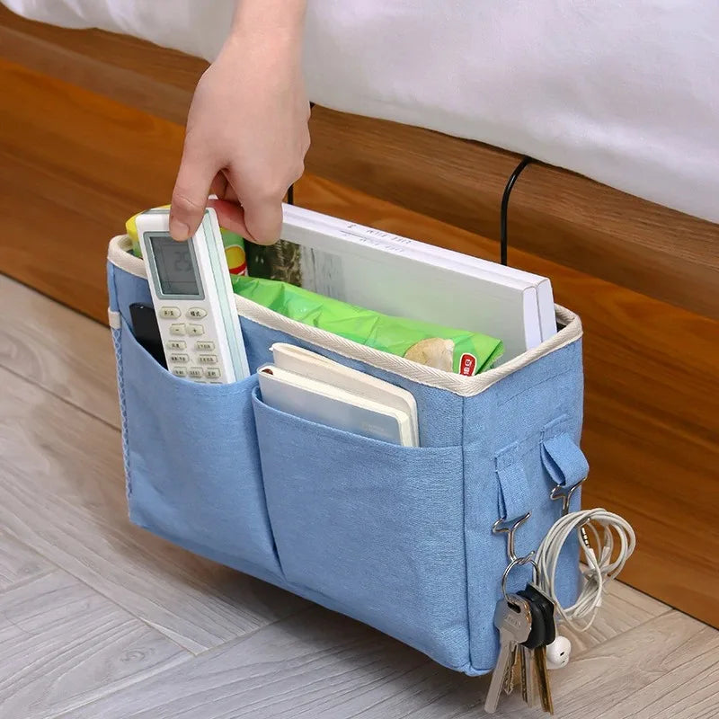 A hand places a white digital device into a light blue fabric storage rack with a hanging basket and keys.