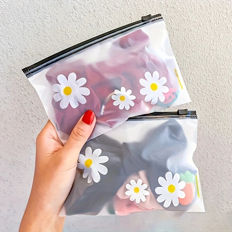A hand holds a clear plastic zipper storage bag featuring a white daisy pattern against a light background.