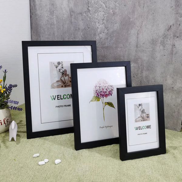 Three black photo frames display floral and welcome designs on a light green surface.