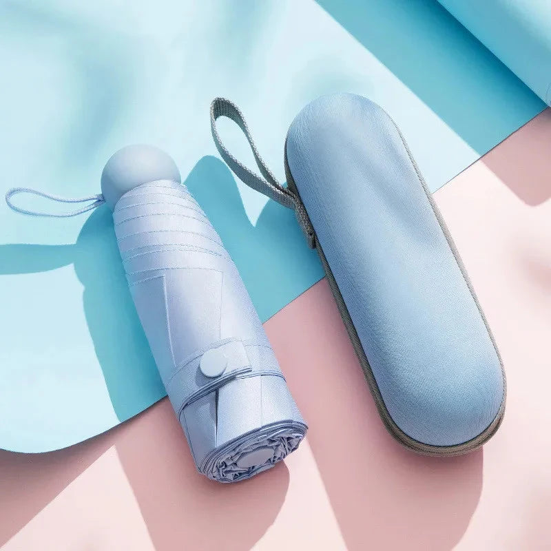 A light blue mini travel umbrella with a fabric sleeve is shown on a pink background.