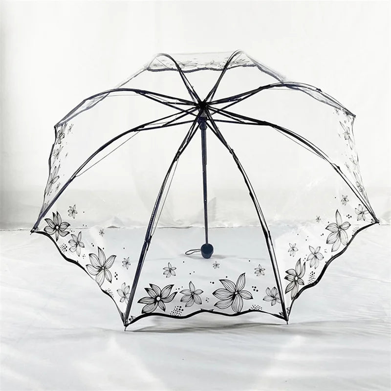 A clear, retro transparent folding umbrella with a black frame and floral pattern rests on white bedding.