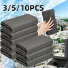 A stack of gray reusable microfiber cleaning cloths is shown next to a hand, set against a scenic outdoor background.