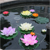 A collection of artificial lotus flowers in various shades of pink, yellow, and purple floating on dark water.