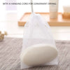 A white bulk soap net bag with a hanging cord, containing a bar of white soap, resting on a gray fabric.