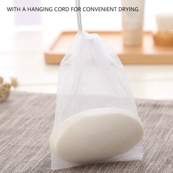 A white bulk soap net bag with a hanging cord, containing a bar of white soap, resting on a gray fabric.