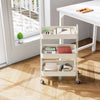 A white metal rolling storage cart with three tiers holds office supplies and electronics on a wooden floor.