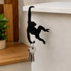 Black monkey shaped wooden key hanger decoration mounted on a white shelf.