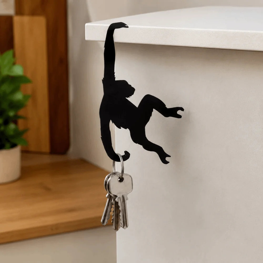Black monkey shaped wooden key hanger decoration mounted on a white shelf.
