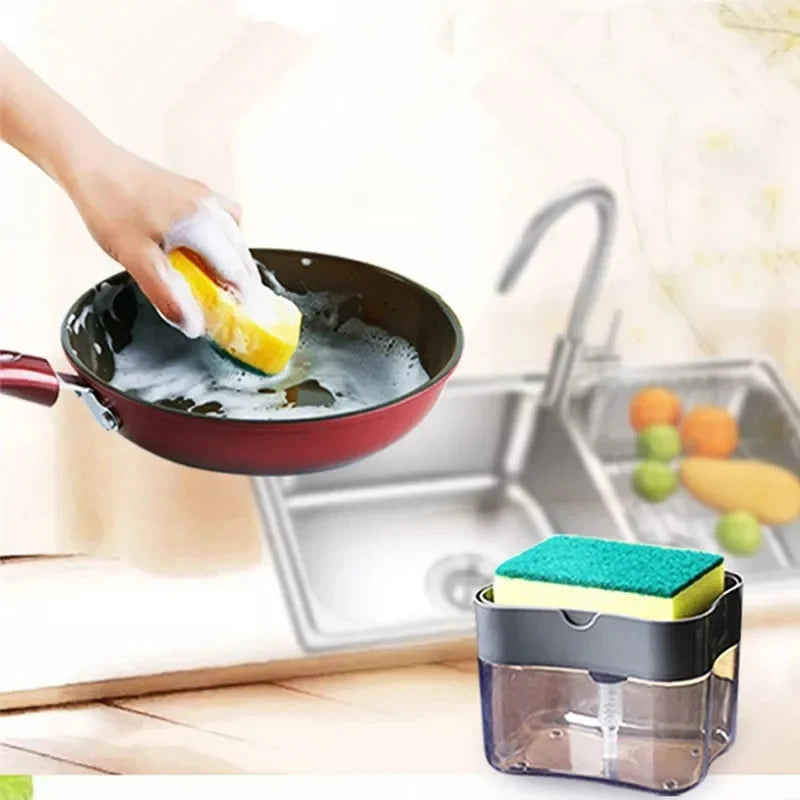 A hand is using a sponge to wash a yellow fruit in a dark pan, with a clear container holding a green sponge nearby.