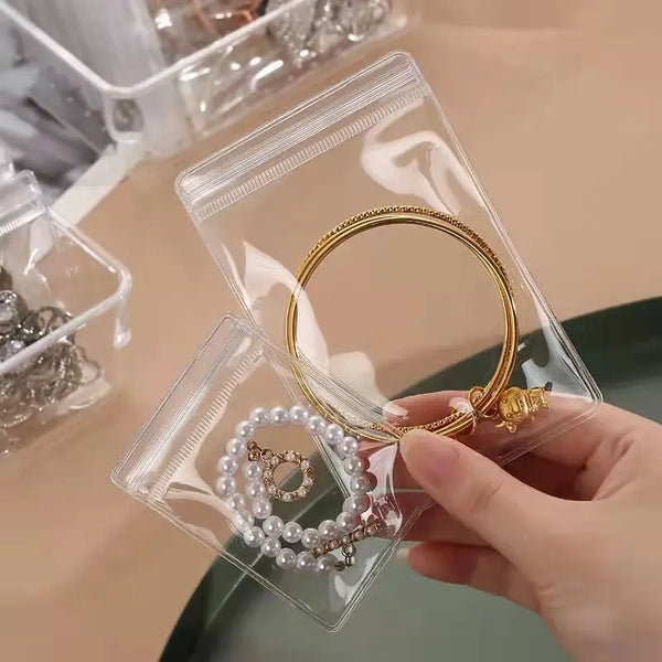 Two clear PVC zip lock jewelry pouches containing gold and pearl rings being held by a hand.
