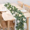 A white floral garland featuring roses and eucalyptus greenery displayed on a wooden table.