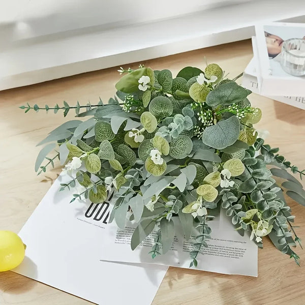 A lush bouquet of artificial eucalyptus flowers in various shades of green and white on a white background.