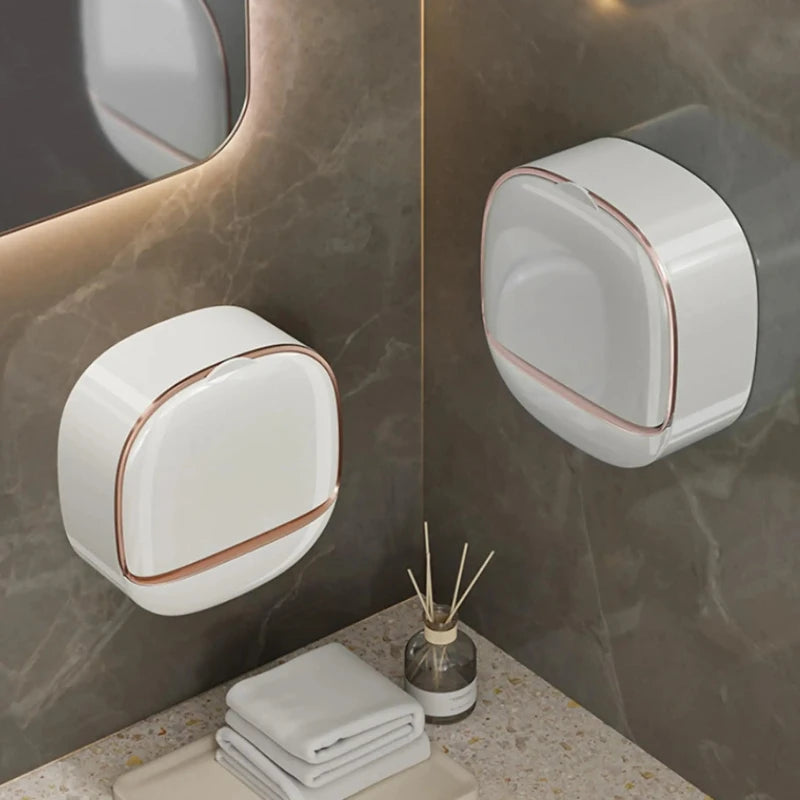 A white wall-mounted soap holder with a lid is displayed against a marble background.