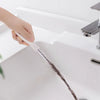 A hand is using a flexible drain cleaning tool to clear a sink drain.