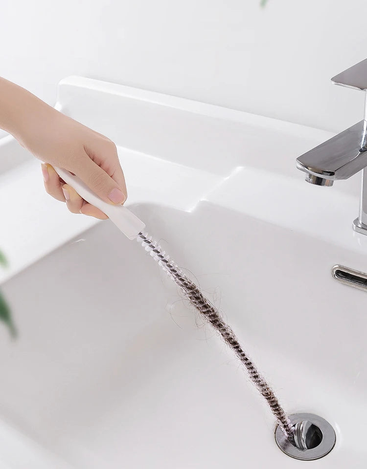 A hand is using a flexible drain cleaning tool to clear a sink drain.