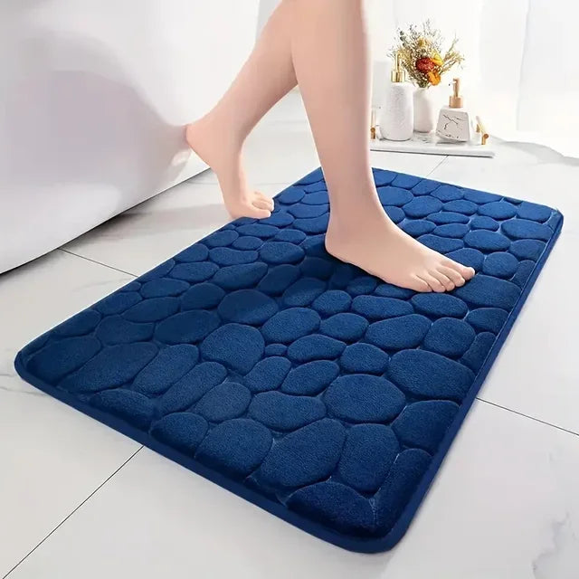 A dark blue, textured 3D non-slip bathroom doormat placed on a white tiled floor.