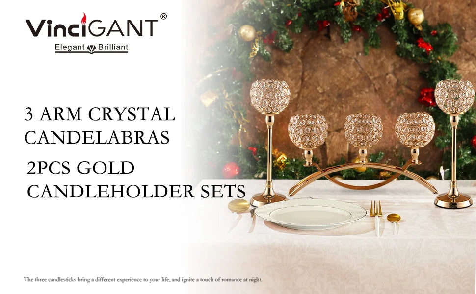 A set of three gold crystal candelabras and candleholders displayed on a table with greenery in the background.