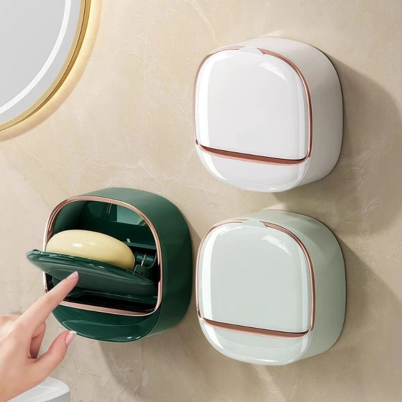 A wall-mounted soap holder in white and green ceramic with a lid, shown against a beige wall.