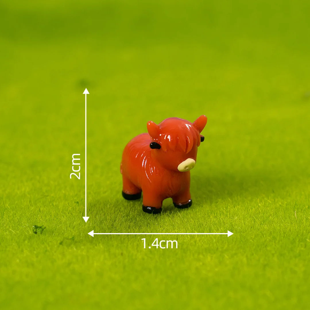 An orange resin figurine of a Highland cow placed on green felt with measurement lines.