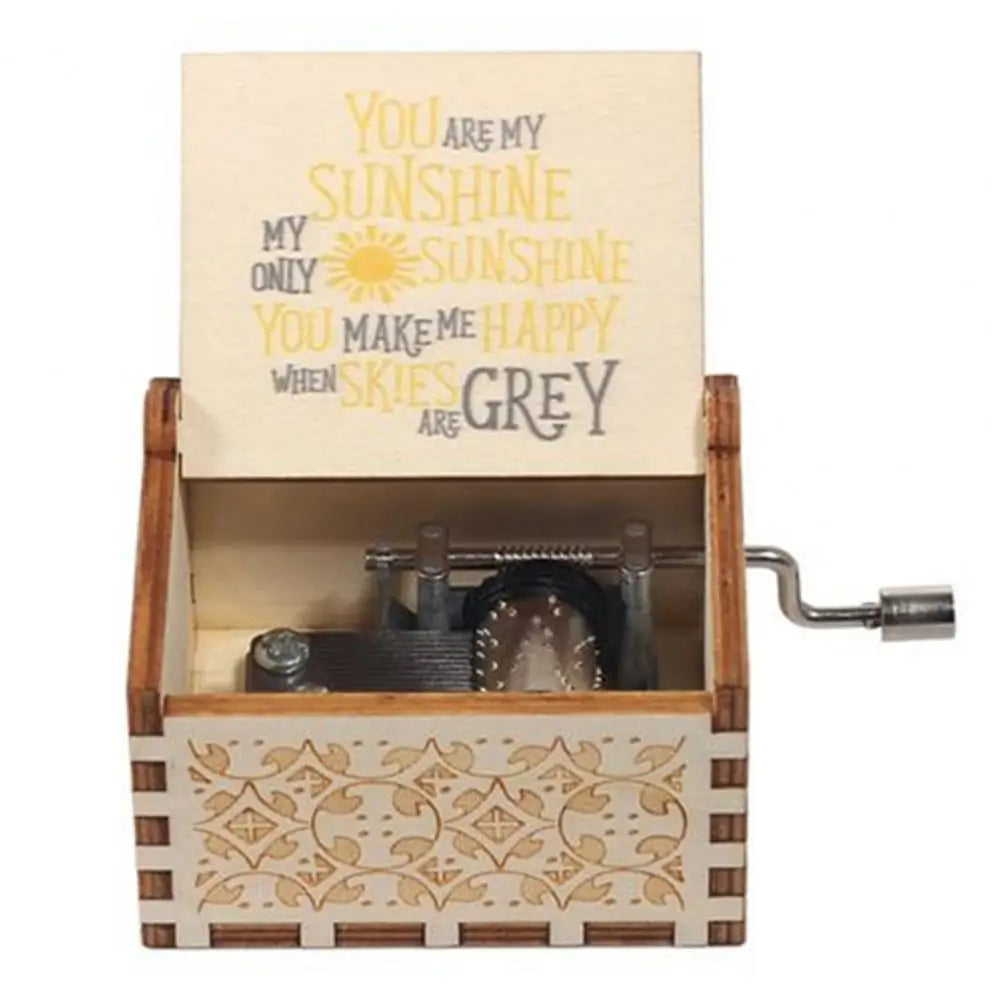 A mini wooden music box with a hand crank and a lid featuring text about sunshine and grey.