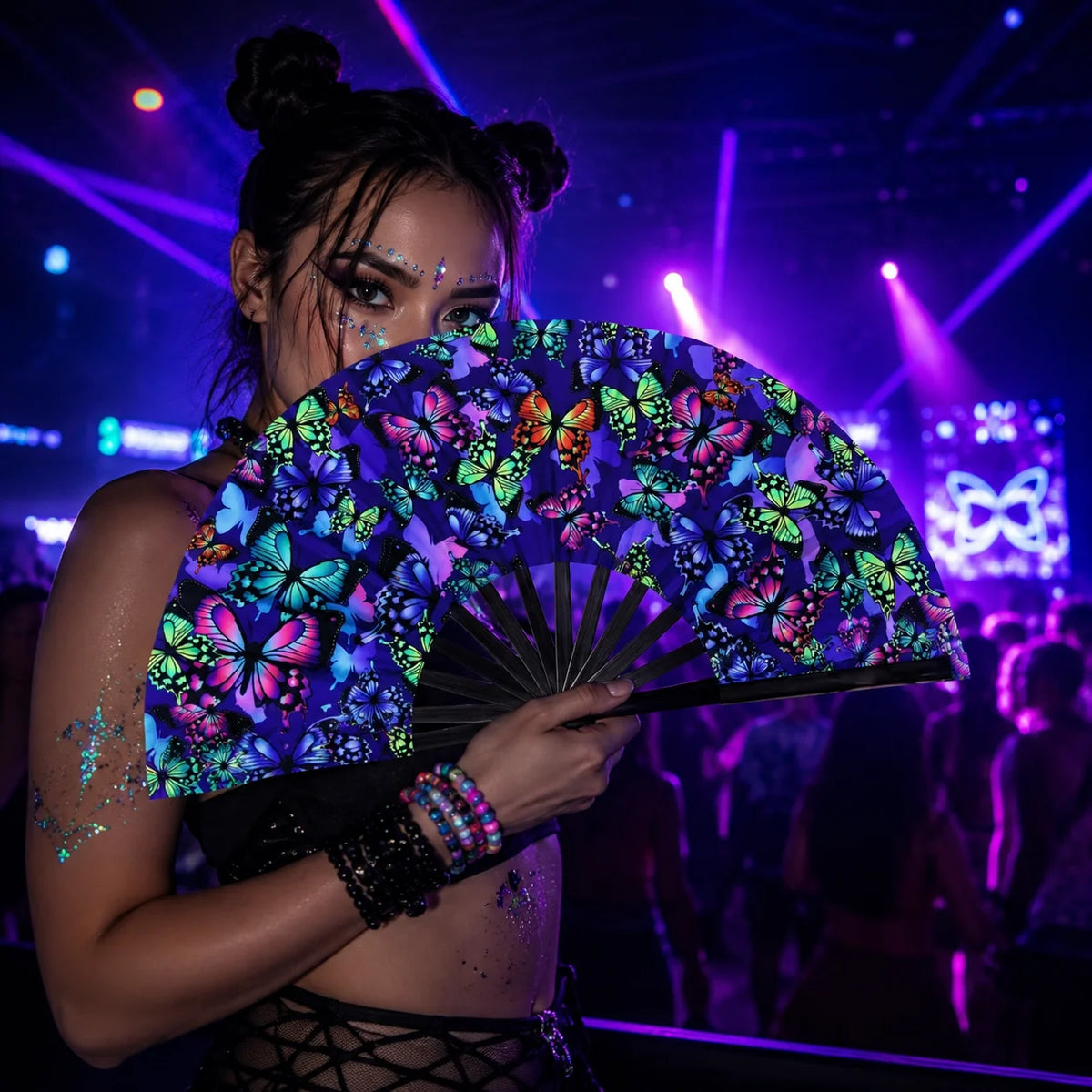A woman holds an open holographic gradient rave hand fan with vibrant floral patterns under stage lights.