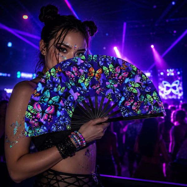 A woman holds an open holographic gradient rave hand fan with vibrant floral patterns under stage lights.