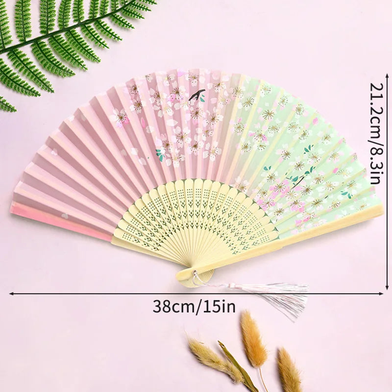A pink and green lace fabric folding hand fan displayed on a light purple background.