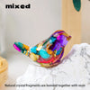 A colorful glass bird statue made from natural crystal fragments and resin resting on a white marble surface.
