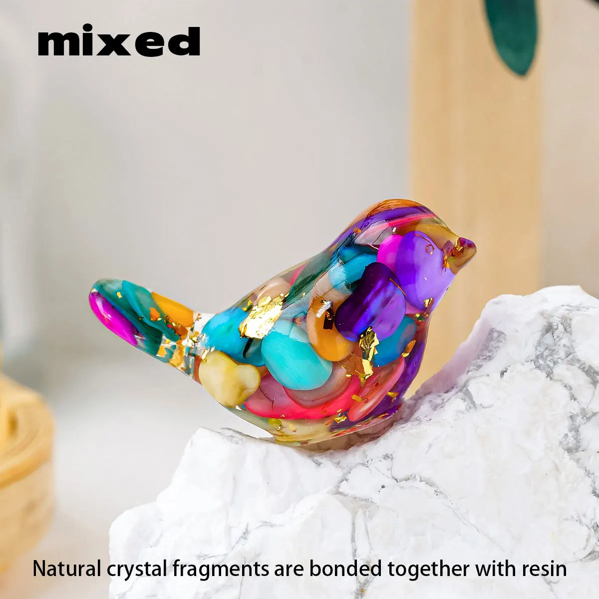 A colorful glass bird statue made from natural crystal fragments and resin resting on a white marble surface.