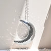 A silver mosaic moon pendant hangs against a light wall, casting a bright shadow.