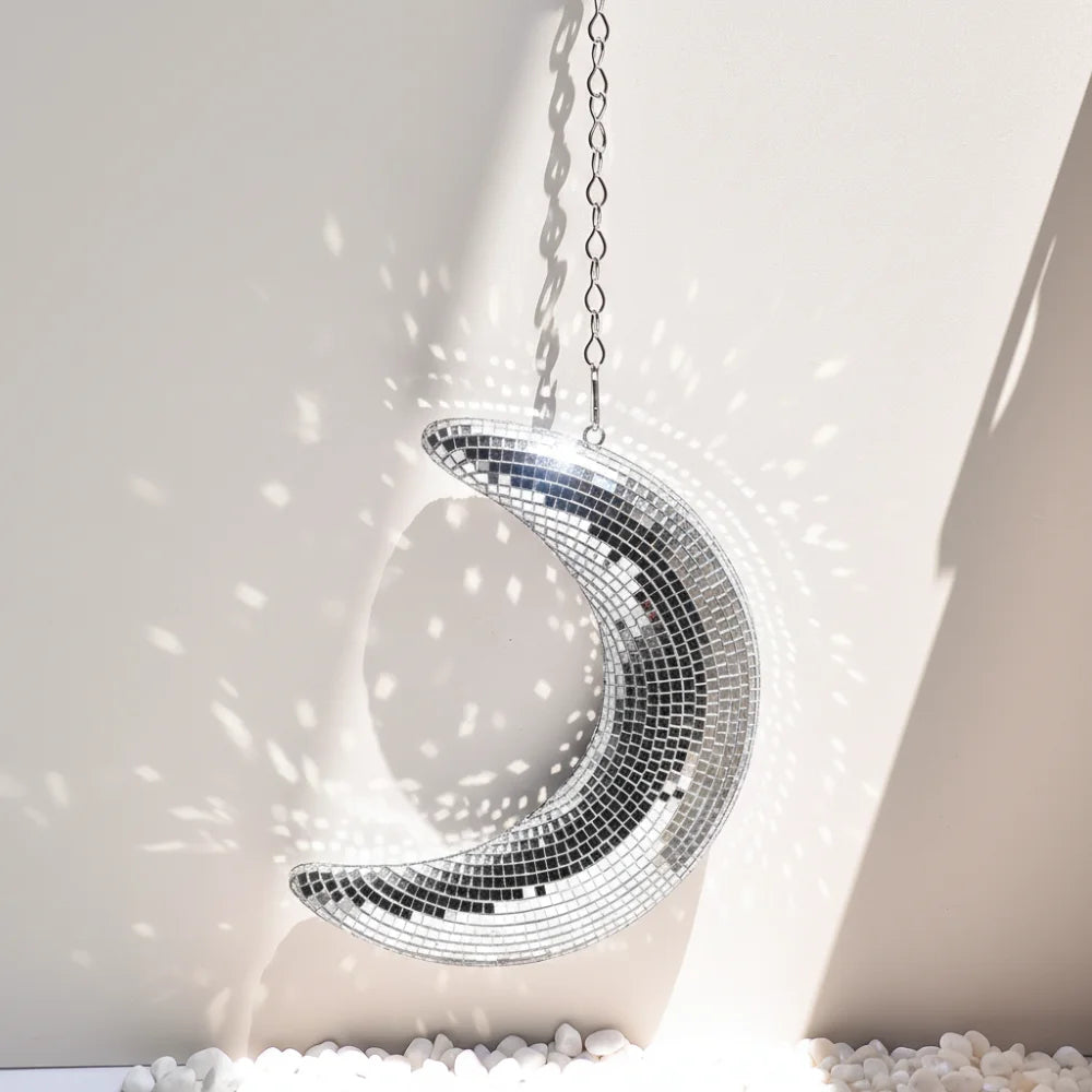 A silver mosaic moon pendant hangs against a light wall, casting a bright shadow.