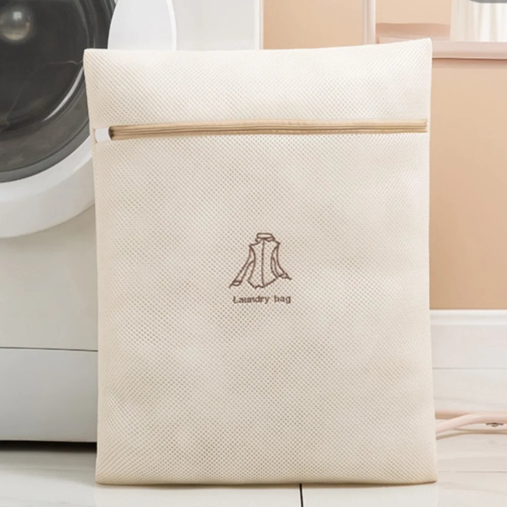 A cream-colored reusable zippered laundry bag with a light wood zipper pull resting on a white surface.