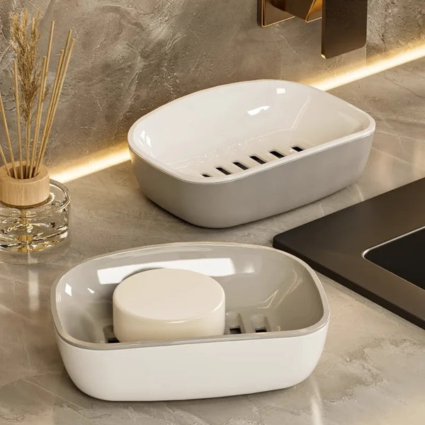 A white double-layer draining soap dish with a non-slip base is shown on a marble countertop.