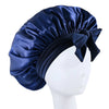 A navy blue silky satin sleep bonnet tied with a bow displayed on a white mannequin head.