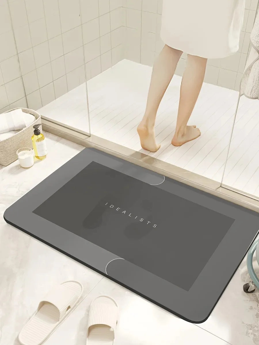 A dark gray diatomaceous earth absorbent bath mat is placed on a white tiled surface next to a glass shower enclosure.