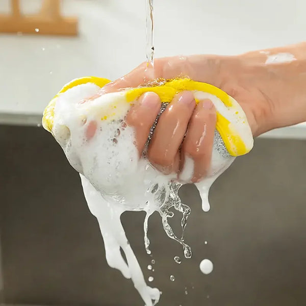 A hand is squeezing a yellow reusable double-sided dishwashing sponge under running water.