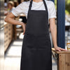 A woman wearing a black chef apron stands in a bright, indoor setting.