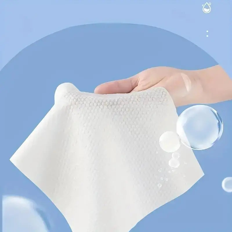 Eine Hand hält ein weißes Einweg-Baumwoll-Gesichtstuch mit sichtbaren Wassertropfen vor einem hellblauen Hintergrund.