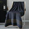 A dark gray bath towel draped over a white stand, featuring gold striped trim.