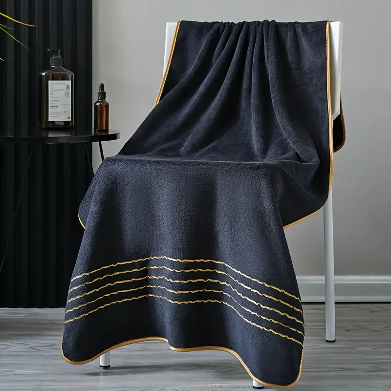 A dark gray bath towel draped over a white stand, featuring gold striped trim.