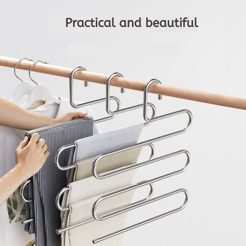 A hand is hanging folded clothes on a multi-layer stainless steel clothes rack mounted on a wooden bar.