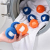 A hand is holding several orange and blue reusable pet hair and lint remover balls inside a washing machine drum.