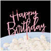 Pink script text spelling Happy Birthday on a cake topper placed on a white surface with white fluffy decorations.
