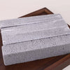 A rectangular stack of gray pumice stone sticks for cleaning household stains, resting on a wooden surface.