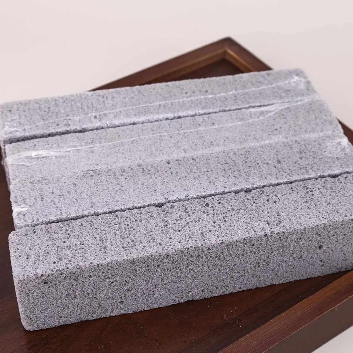 A rectangular stack of gray pumice stone sticks for cleaning household stains, resting on a wooden surface.
